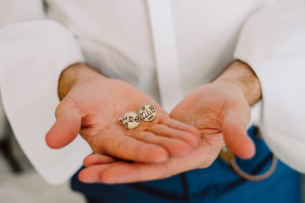 Groom showing handmade suit buttons with the initials of the wedding couple and their wedding date at Altes Weingut Moebus in Siefersheim