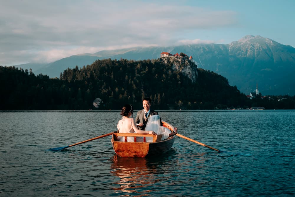 Wedding couple on a boat at lake Bled with a stunning background and the Church of the Assumption of the Blessed Virgin Mary in the background